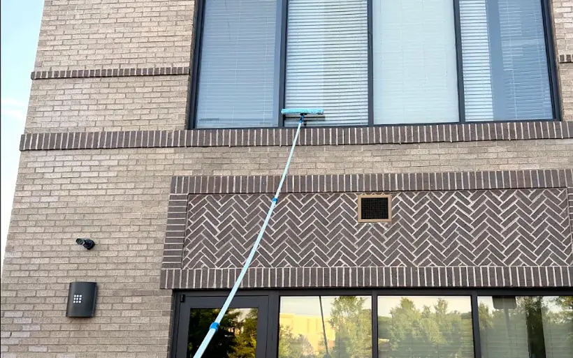 A Faithful Finish team member washing second-story commercial windows with an extension pole